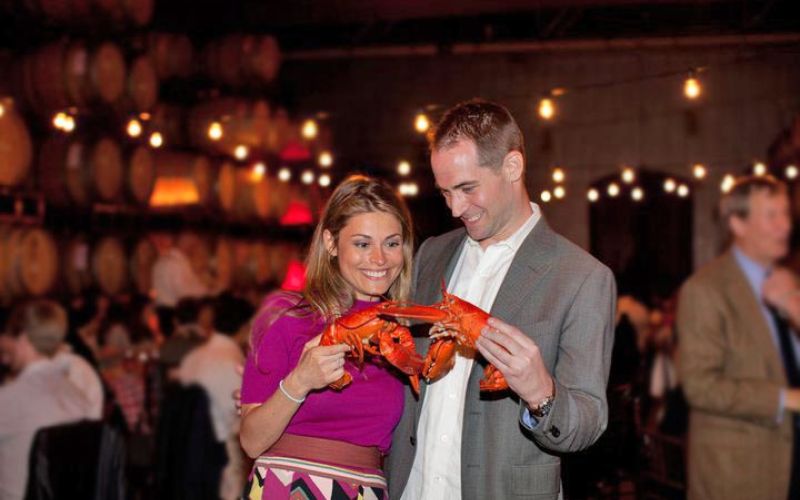 engaged couple holding steamed lobsters at catered wedding rehearsal dinner in San Francisco Bay Area winery cellar