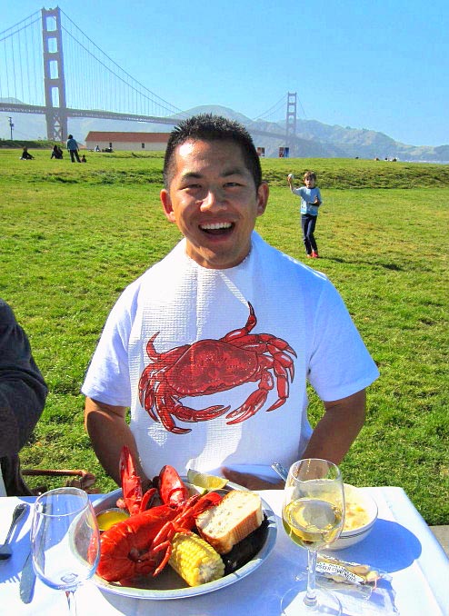 smiling young man wearing lobster bib in front of lobster clambake plate at catered private event at San Francisco's Golden Gate Park