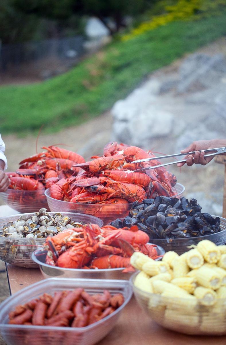 closeup of Sam's Lobster Clambake buffet table showing large bowls of fresh steamed lobsters, steamed clams and mussels, roasted corn on the cob and andouille sausage