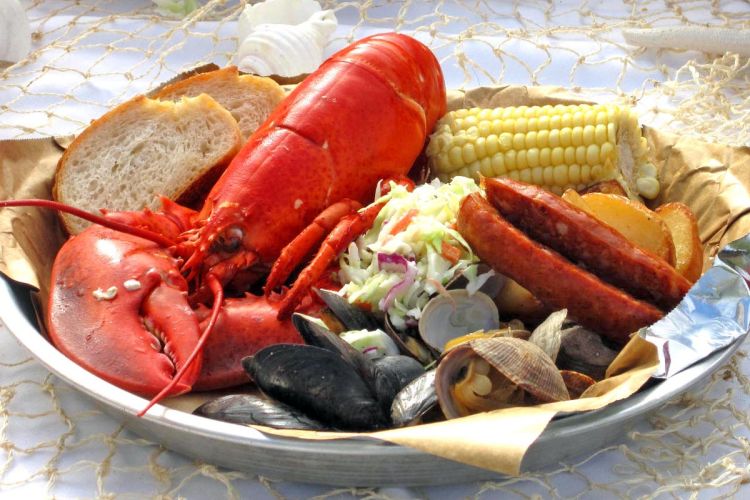 closeup of Sam's Lobster Clambake dinner plate with a whole steamed fresh lobster, steamed clams and mussels, corn on the cob, andouille sausage, fresh bread and cole slaw